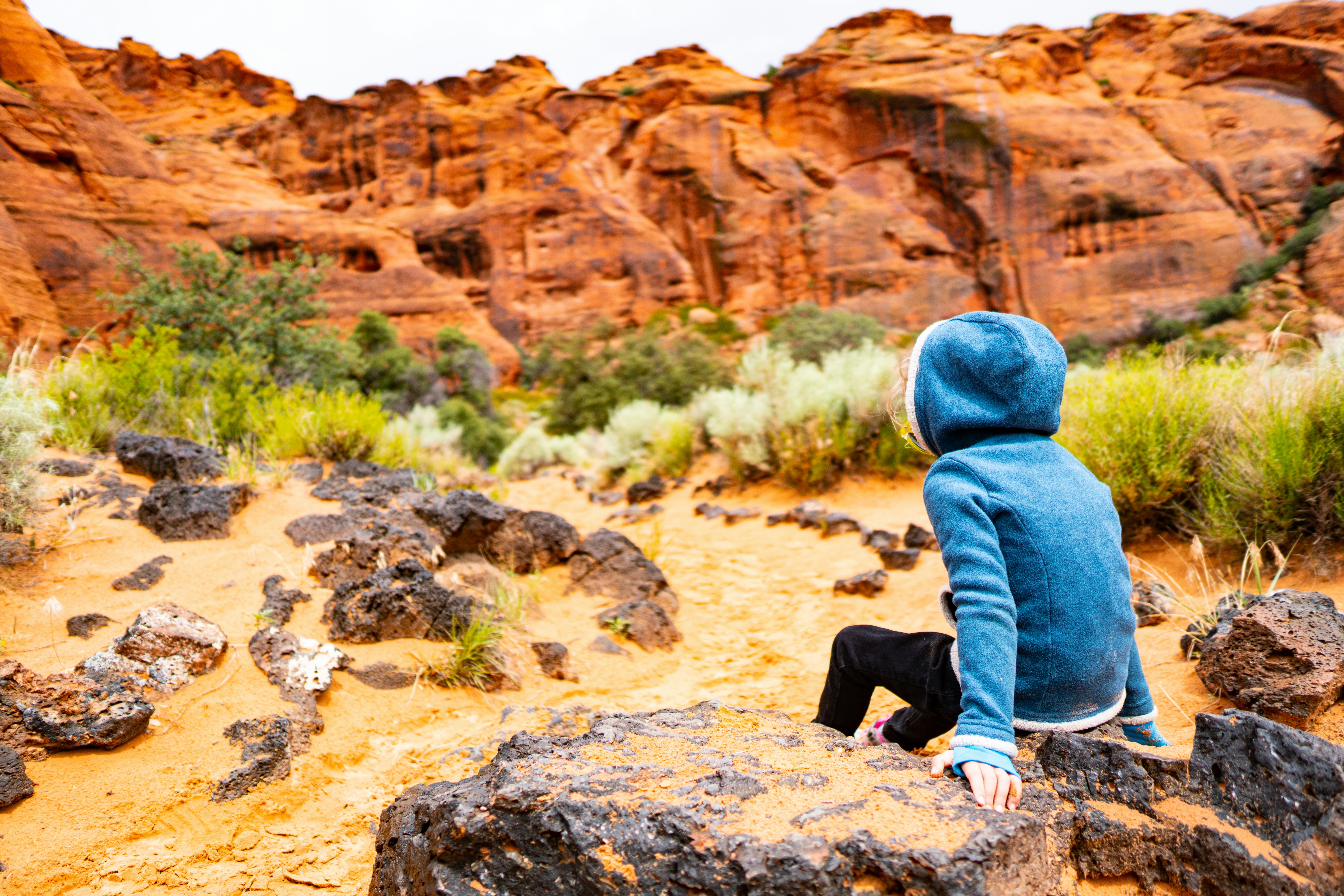 person wearing hoodie sitting on rock facing the rocky mountain